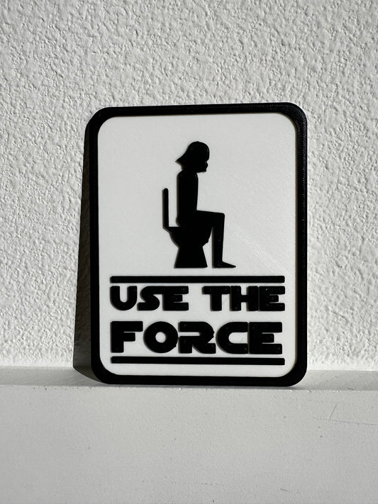 picture of a funny sign showing a person wearing a stormtrooper inspired helmet sitting on the toilet with caption of "Use The Force"